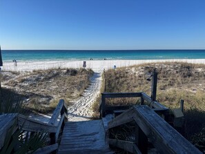 A wooden boardwalk leading to a sandy beach with a clear blue sky.