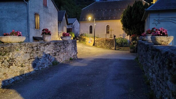 Un carrer de vila amb parets de pedra, cases i una església amb campanar.