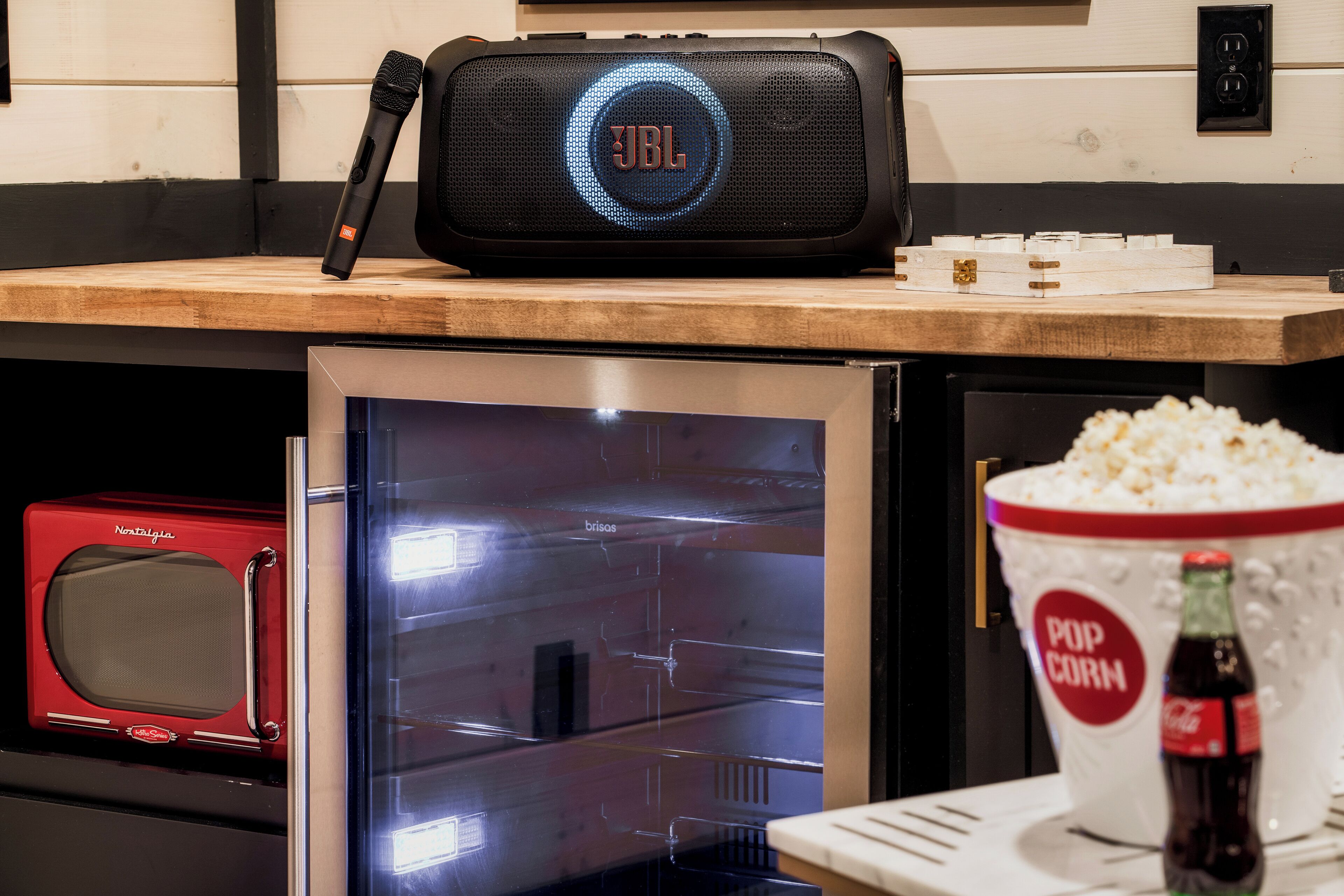 Et tekøkken med mikrobølgeovn, køleskab, en popcorn-spand, en Coca-Cola flaske og en JBL-højttaler.