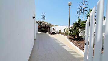 A sunlit corridor with a tiled floor, a white fence, and a row of sun loungers.