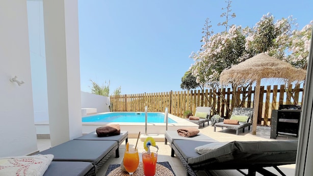 A poolside area with lounge chairs, a table with drinks, and a wooden fence. - Wellness Apartment with Sauna & Private Pool - Duna Parque Group (Odemira)
