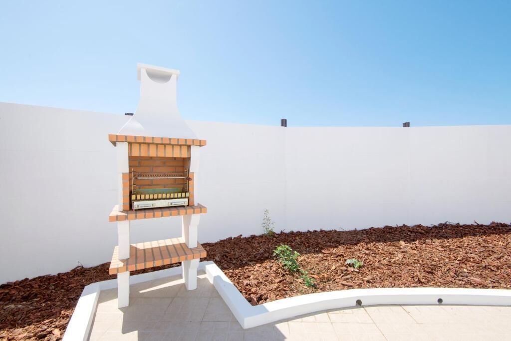 Una parrilla con chimenea, rodeada por un muro blanco y un cantero con acolchado.