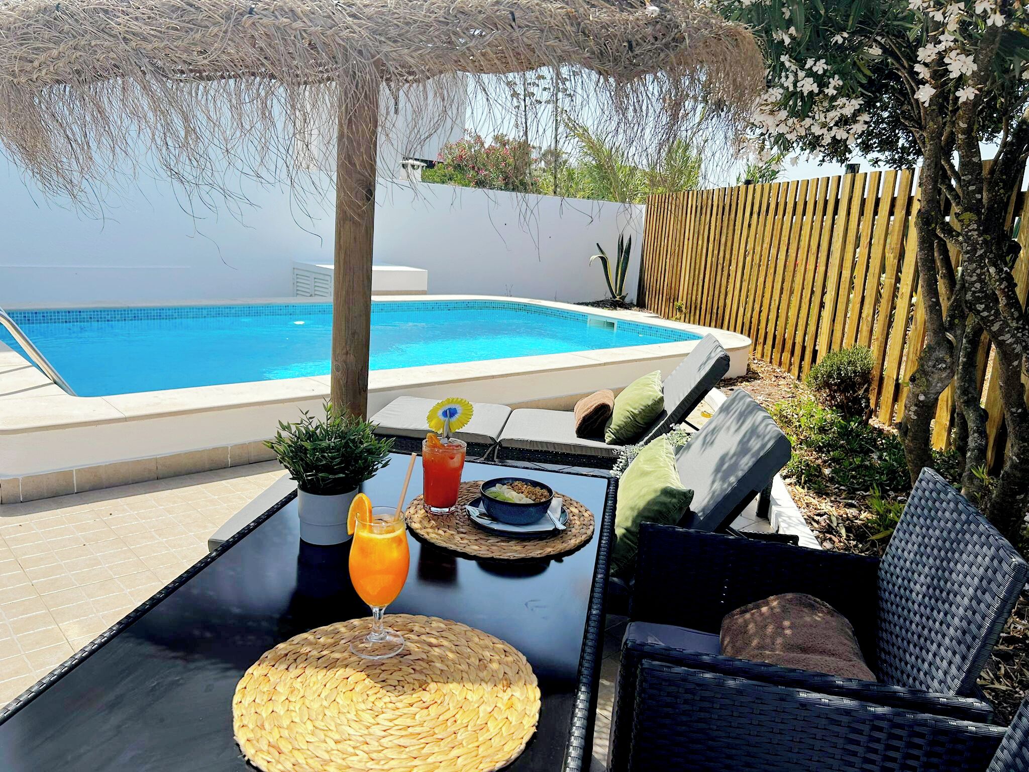 Un espace aménagé au bord de la piscine, avec une table dressée pour deux personnes, une boisson et un bol de collations.