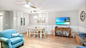 Ein geräumiges Wohnzimmer mit Essbereich, weißen Schränken, Deckenventilator, Flachbildfernseher und Holzboden.