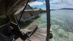 Overwater bungalows with wooden walkways extending into clear water, surrounded by lush greenery. - Arborek Dive Homestay  (Arborek)