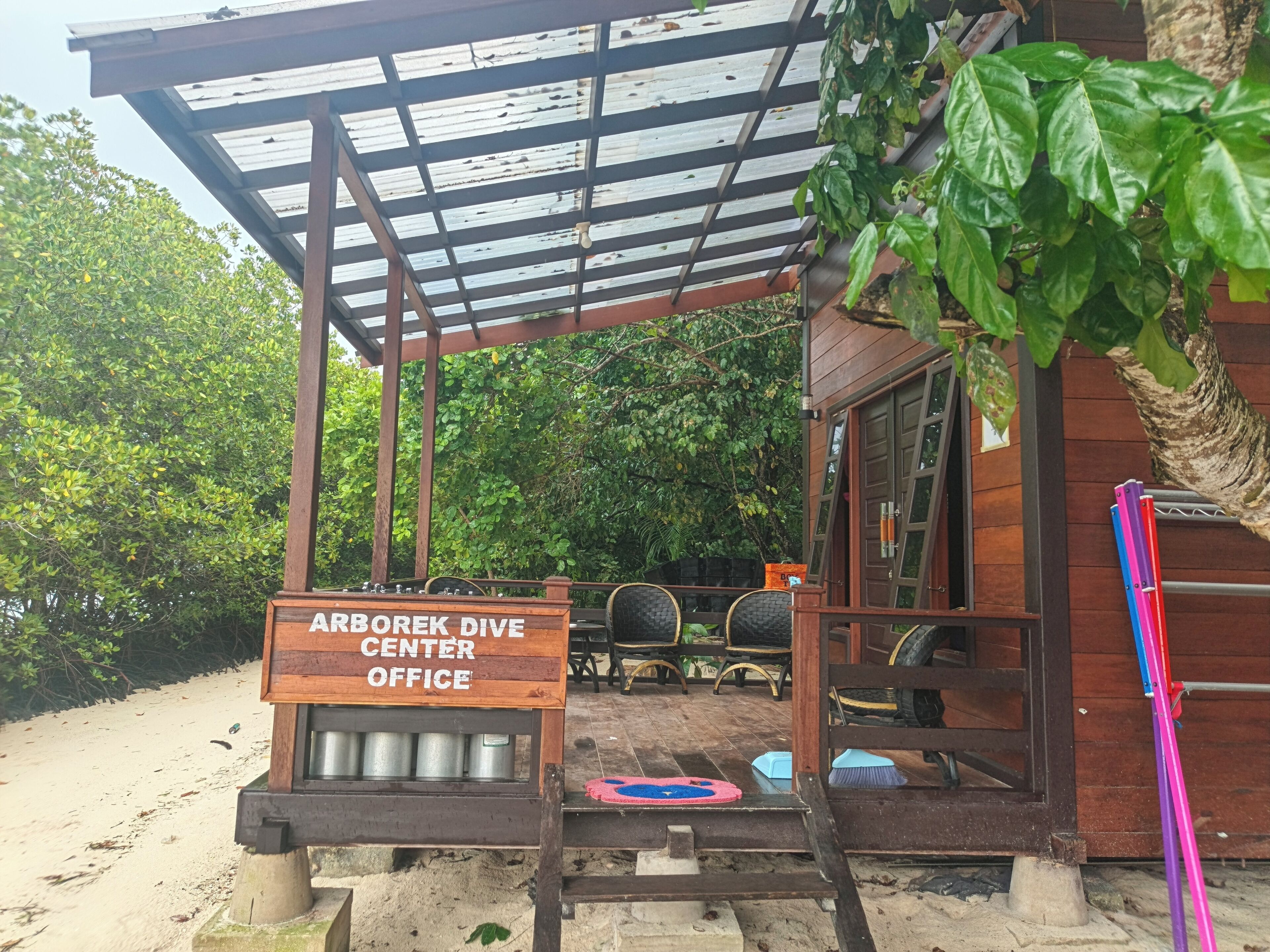 Une structure en bois située à l’extérieur, sur laquelle est apposée une enseigne indiquant « Bureau du centre de plongée Arborek ».