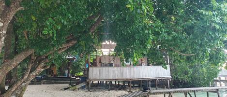 A wooden structure on stilts over a sandy beach, surrounded by dense green foliage.