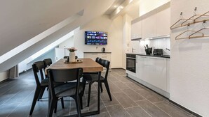 A modern kitchen with a dining area, featuring a large TV mounted on the wall, a wooden dining table, and black chairs. - book2stay 2.5-room apartment #8 Säntis up to 6 people (St. Gallen)