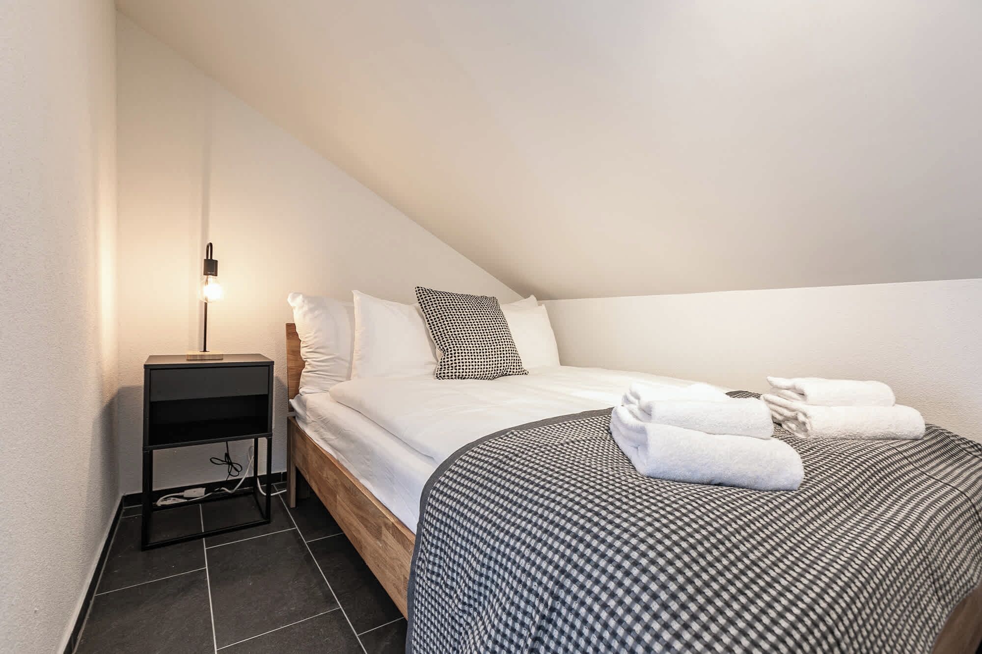 A bedroom with a bed, bedside table, lamp, and towels.