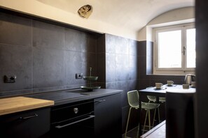 A modern kitchen with dark tiles, a wooden countertop, and a window with a view.