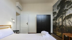 Ett hotellrum med en säng, en garderob, en tavla och ett litet bord.