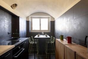 A compact kitchen with dark tiles, a window, a table with chairs, and a wooden counter.