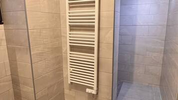 A shower with a glass door, beige tiled walls, and a white towel rack.