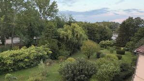 A well-maintained garden with various shrubs and trees, a paved pathway, and a street visible in the background. - Charming, quiet house, fully equipped for a family or professional getaway! (Casseneuil)