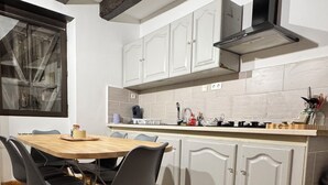 A kitchen with a hexagonal tile floor, wooden dining table with chairs, white cabinets, and a black range hood. - Charming, quiet house, fully equipped for a family or professional getaway! (Casseneuil)