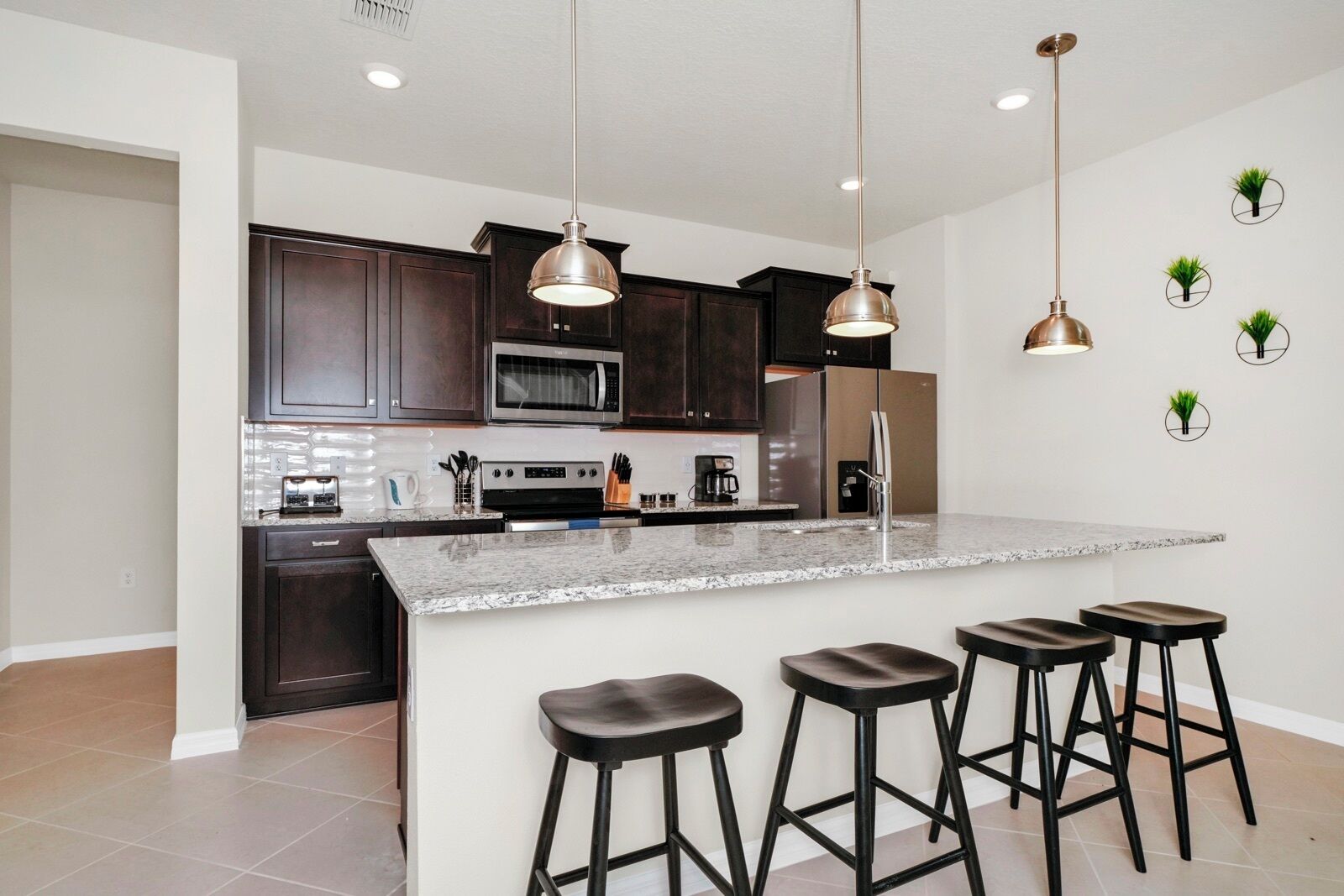 A modern kitchen with dark wood cabinets, stainless steel appliances, a granite countertop, and three bar stools.