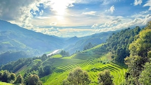 A panoramic view of terraced fields in a valley with a mountain range in the background and a partly cloudy sky. - Chai Eco House Mu Cang Chai (Mu Cang Chai)