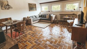 A cozy living room with a tiled floor, a sofa, a dining table with chairs, and a television. - Gemütliche individuelle Wohnung oberhalb der Oker-Talsperre. (Schulenberg im Oberharz)