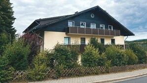 A two-story building with a dark roof and beige walls, surrounded by dense greenery. - Gemütliche individuelle Wohnung oberhalb der Oker-Talsperre. (Schulenberg im Oberharz)