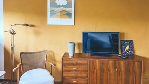 A room with a wooden desk, a chair, a television, and a framed picture on the wall. - Gemütliche individuelle Wohnung oberhalb der Oker-Talsperre. (Schulenberg im Oberharz)
