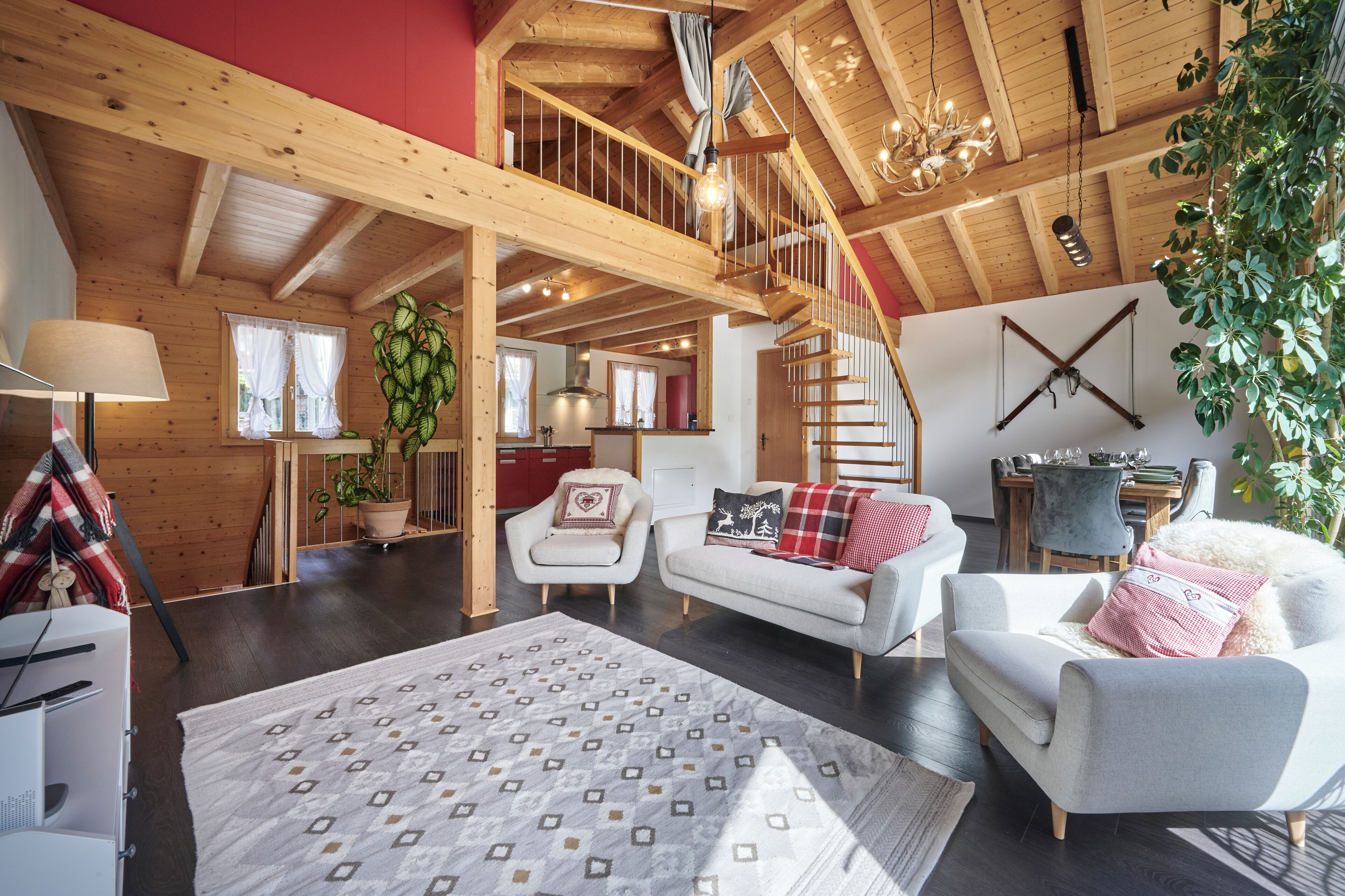Een ruime woonkamer met een hoge plafond, houten balken, een trap en een eethoek op de achtergrond.