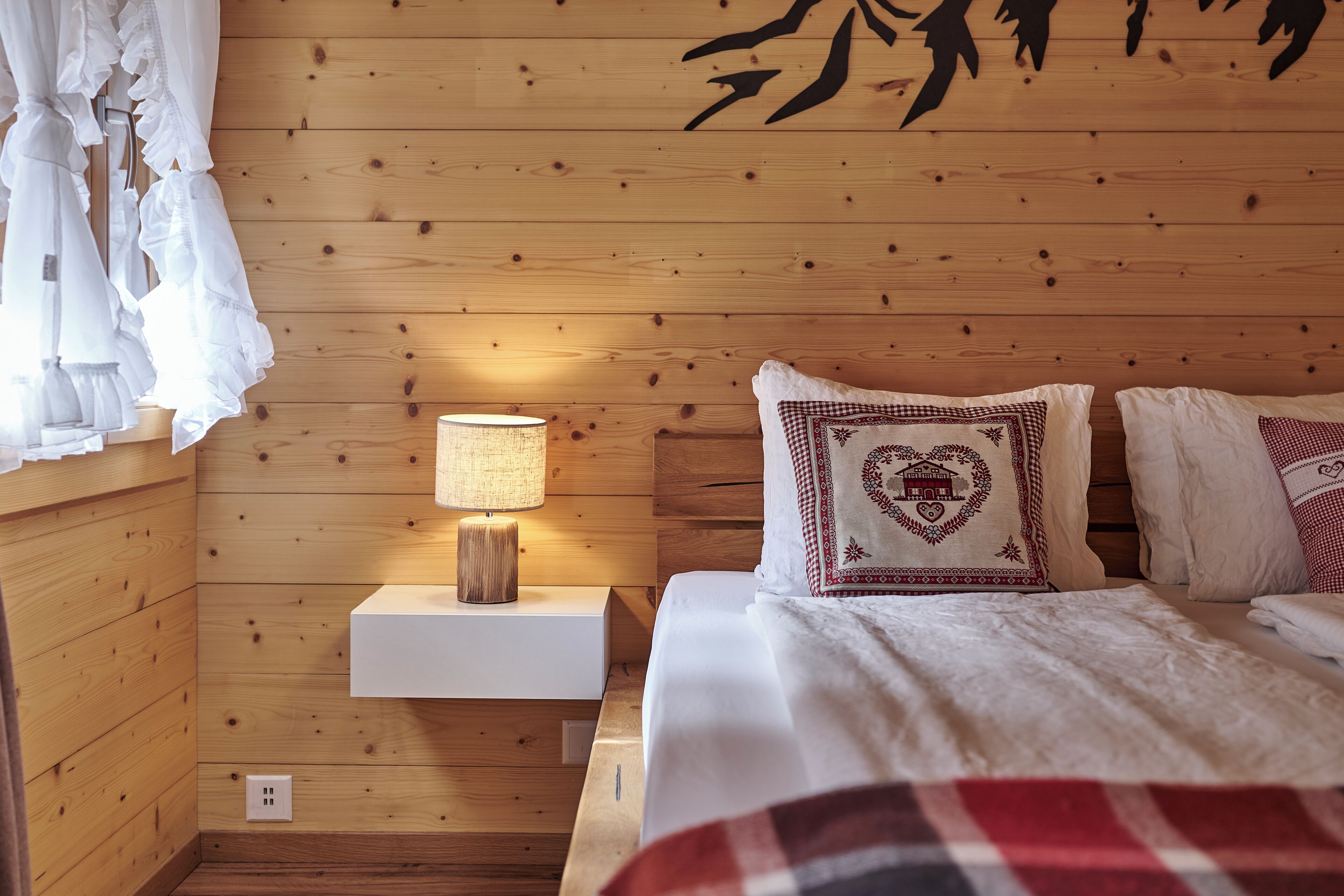 Une pièce aux murs lambrés, avec un lit, une table de chevet dotée d’une lampe et des coussins décoratifs.