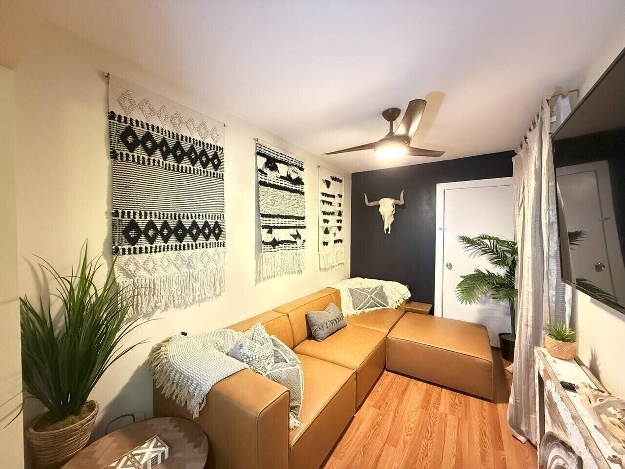 A modern living room with a sectional sofa, wall art, a ceiling fan, and a door with a cow skull decoration.