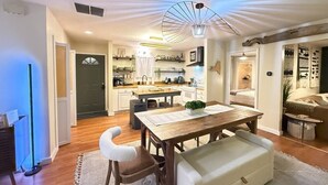 A modern kitchen with wooden cabinets, a dining area with a wooden table and chairs, and a ceiling light fixture.