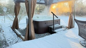 A hot tub under a glass canopy with curtains, surrounded by snow.