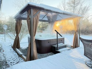 Un jacuzzi bajo un techo de cristal con cortinas, rodeado de nieve.