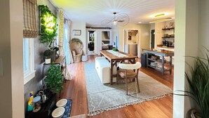A spacious living area with a wooden floor, a dining table, and a kitchen in the background.