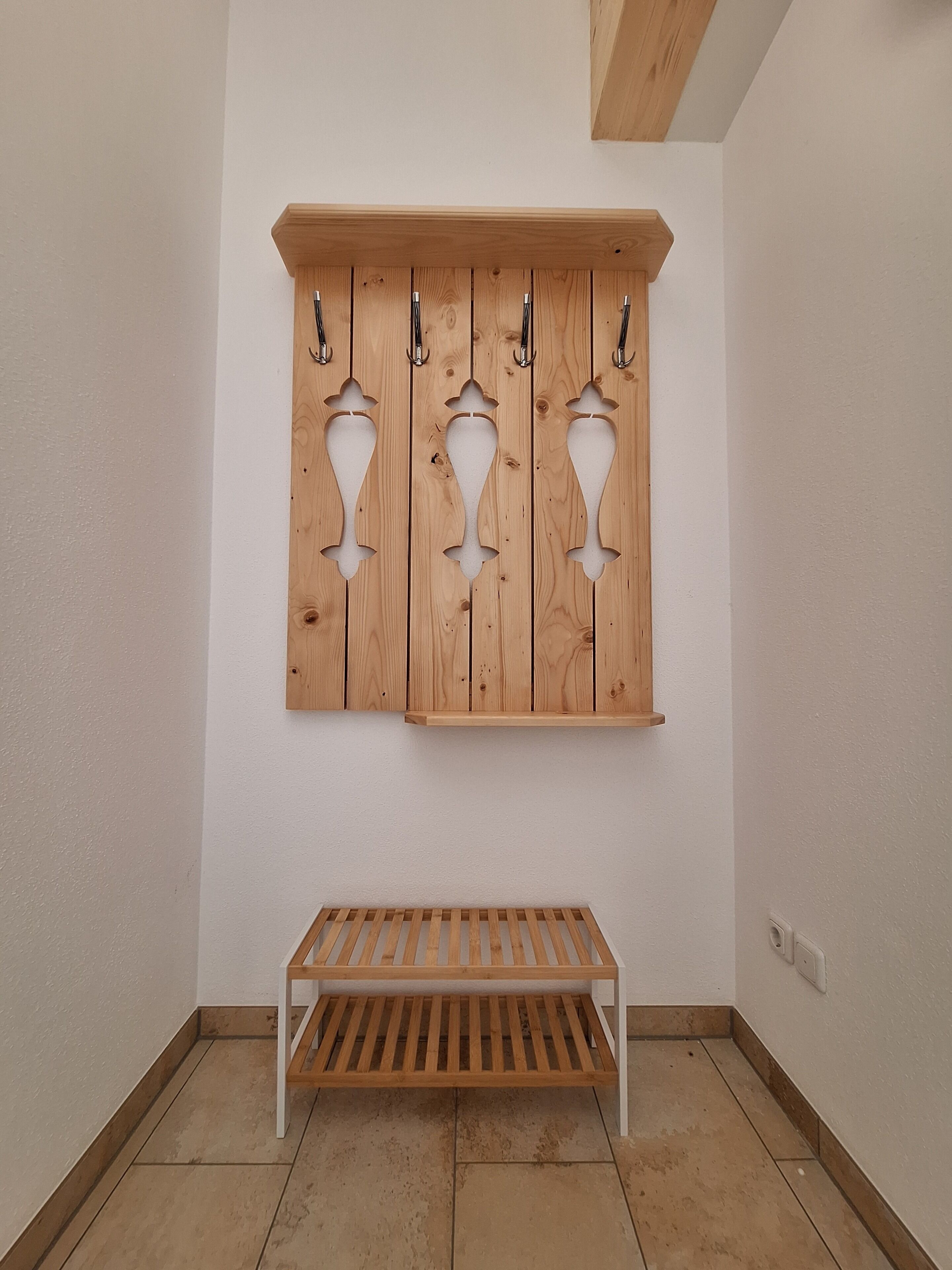 A corner with a wooden bench and a wall-mounted coat rack with three hooks.