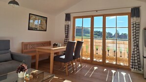 Une pièce spacieuse comprenant une table à manger en bois, des chaises, un canapé et une table basse en verre. Une grande fenêtre, agrémentée de rideaux, offre une vue sur l’extérieur.