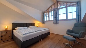 Une chambre à coucher avec un lit, des tables de chevet, une chaise et une fenêtre avec des rideaux.