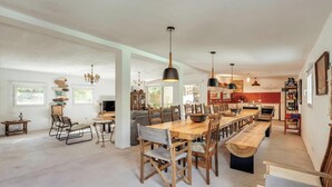 Una cocina amplia con una larga mesa de madera, luces colgantes y un revoque de ladrillo.