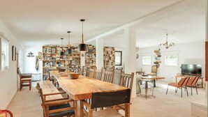 Un amplio salón con una larga mesa de comedor de madera, varias estanterías y un televisor.