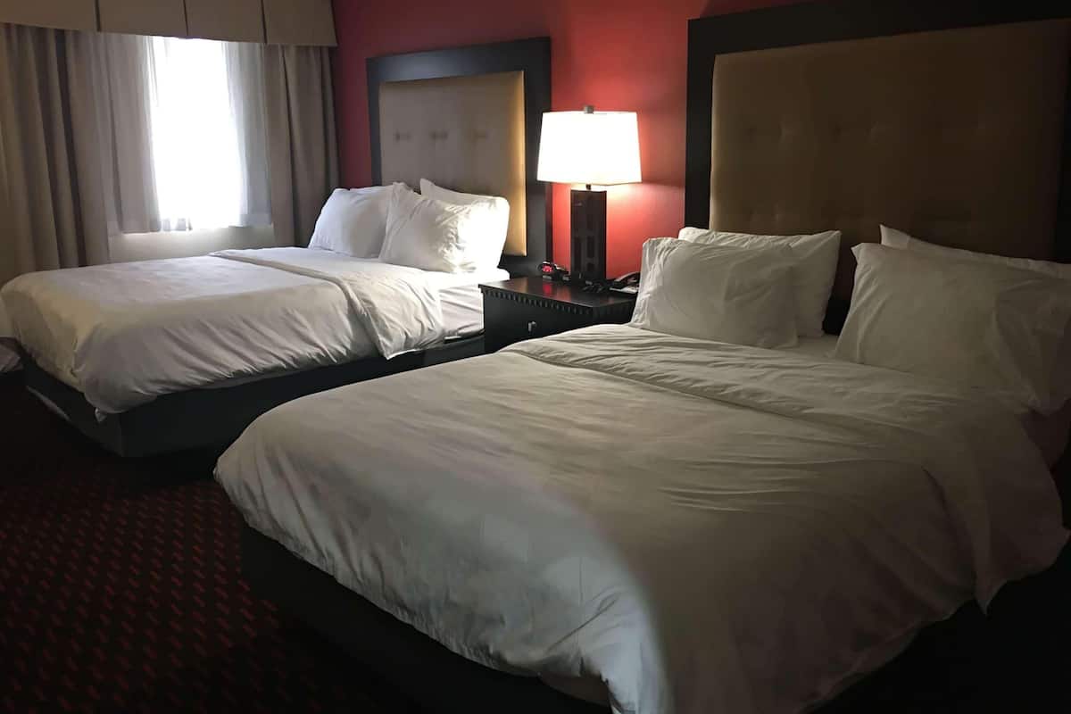 A hotel room with two beds, a nightstand with a lamp, and a window with curtains.