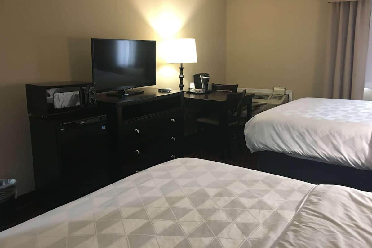 A hotel room with two beds, a television, a desk with a lamp, and a coffee maker.