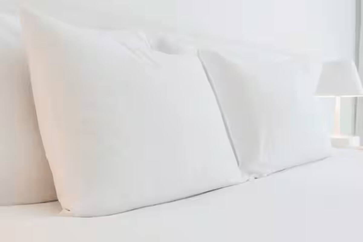A neatly made bed with white bedding and pillows.