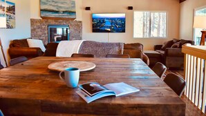 A cozy living room with a wooden dining table, leather sofas, a stone fireplace, and a TV mounted on the wall. - Lake Tahoe Tree House with Panoramic Views of Lake Tahoe (Zephyr Cove)