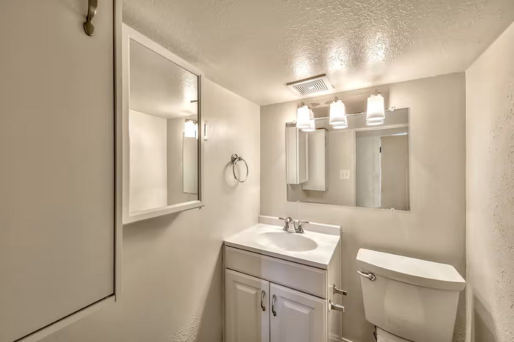 A bathroom with a white sink, mirror, and toilet.