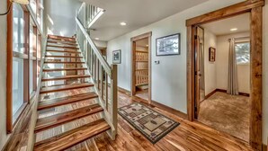 A wooden staircase leading to a second floor, a hallway with a rug, and a door with a view of trees. - Lake Tahoe Tree House with Panoramic Views of Lake Tahoe (Zephyr Cove)
