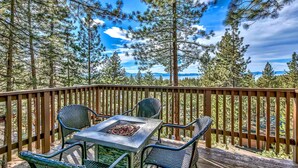 A deck with a table and chairs, surrounded by tall trees and a clear sky. - Lake Tahoe Tree House with Panoramic Views of Lake Tahoe (Zephyr Cove)