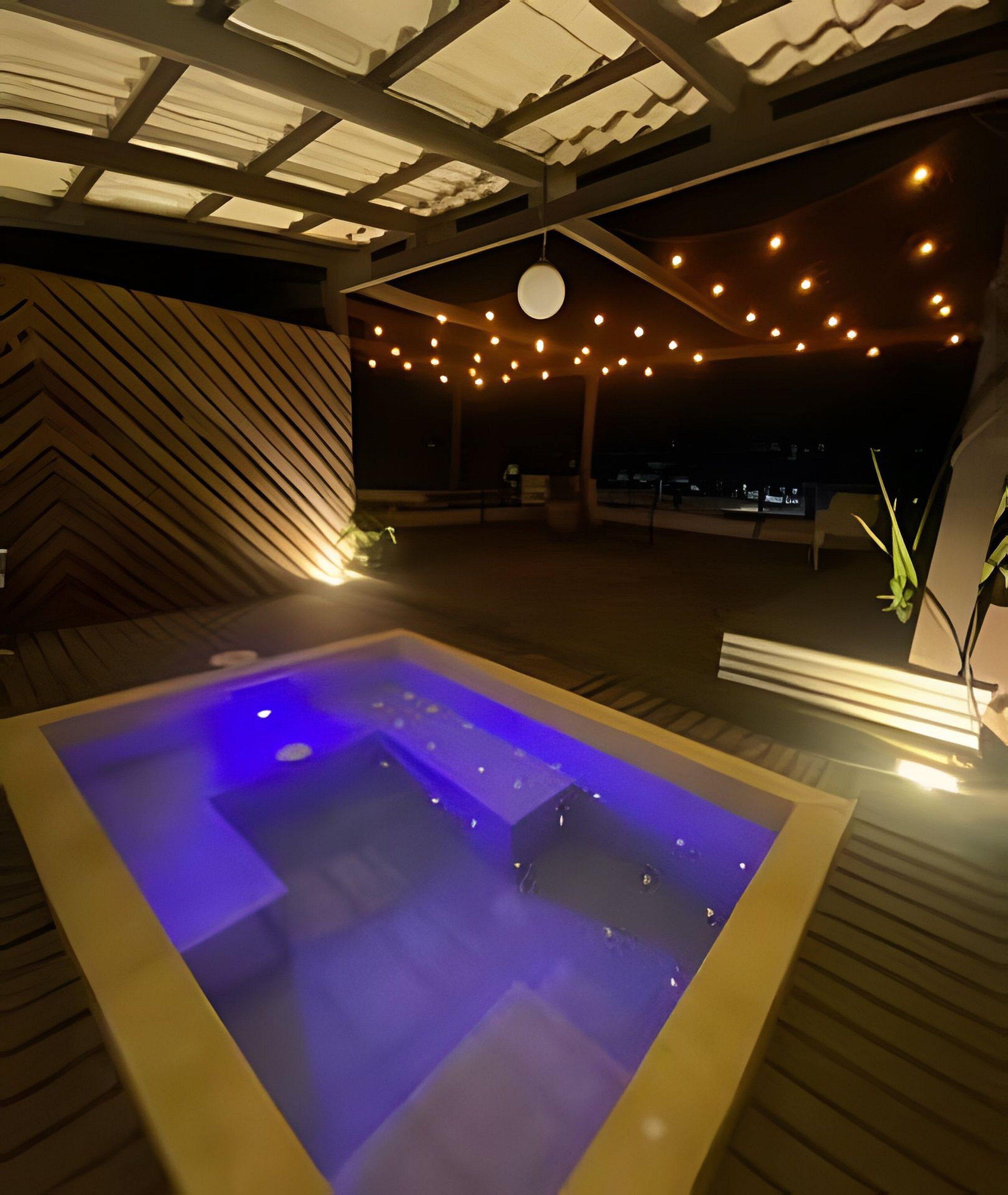 Ein Whirlpool mit blauer Beleuchtung, Holzboden und Lichterkette.