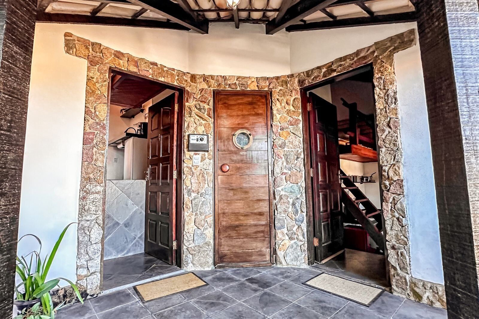 A stone-framed entrance with two doors, a doormat, and a tiled floor.