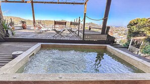 A hot tub with a wooden deck and lounge chairs, overlooking a cityscape. - Villa Rustica (Arraial do Cabo)