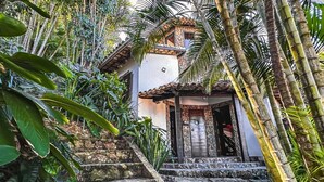 A house with a stone facade, a wooden door, and a staircase leading to the entrance. - Villa Rustica (Arraial do Cabo)