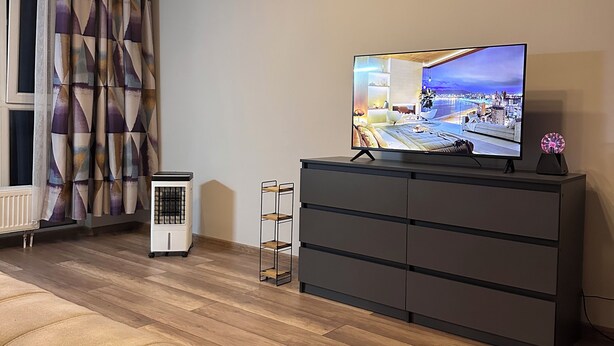 Una sala de estar moderna con un televisor de pantalla plana sobre una cómoda oscura, un radiador y una cortina estampada.