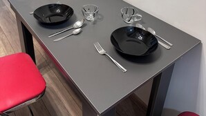 Una mesa de comedor con dos platos negros, cubiertos y recipientes de vidrio transparente.