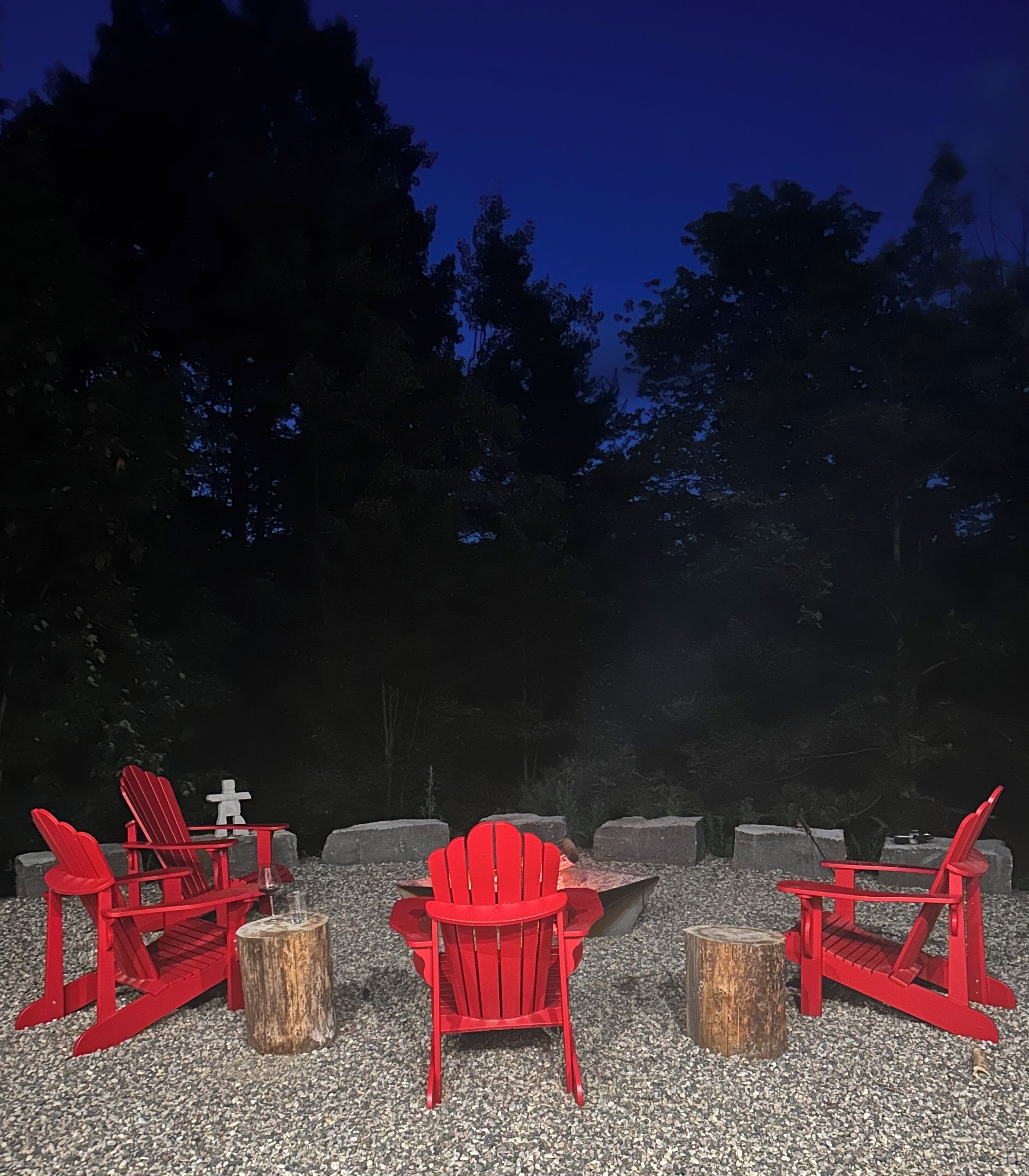 A deck with three red Adirondack chairs, a small table, and a fire pit.